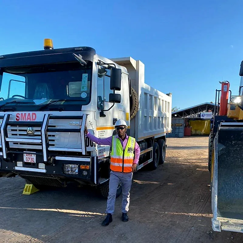 Smad team member wearing a hard hat and high-visibility vest beside a tipper truck